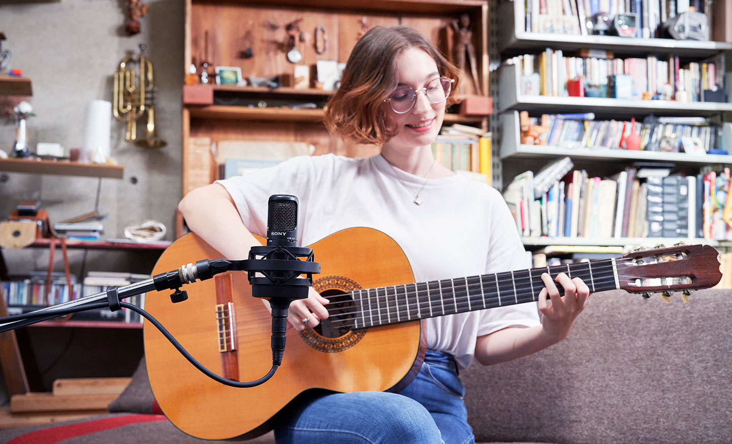  Gambar seorang perempuan memainkan gitar akustik dan merekam dengan mikrofon kondensor Uni-direksional Sony C-80